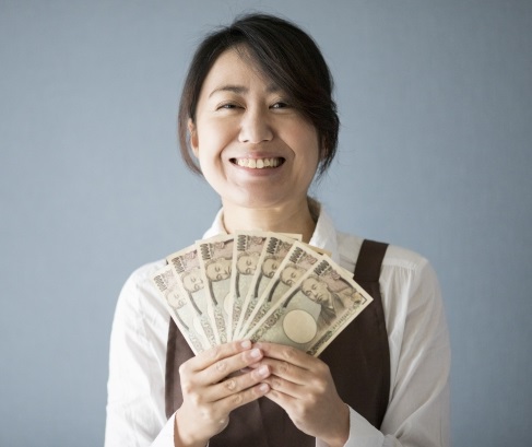 たくさんの一万円札を両手で持って広げている笑顔の女性